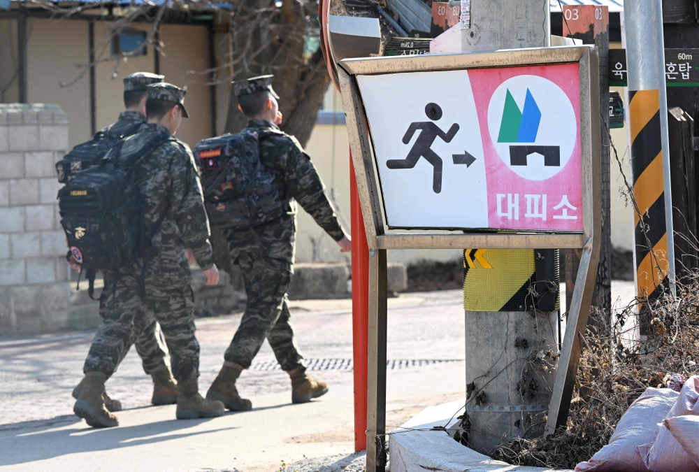 South Korean marines walk past a shelter sign in a village of Yeonpyeong island, near the 'northern limit line' sea boundary with North Korea, on January 6, 2024. (Photo by Jung Yeon-je / AFP)