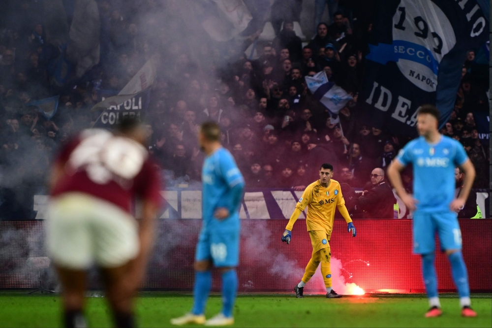 Napoli’s Italian goalkeeper Pierluigi Gollini walks on the pitch past a firework thrown by Napoli's supporters during the Italian Serie A football match Torino vs Napoli at the “Stadio Grande Torino” in Turin on January 7, 2024. (Photo by MARCO BERTORELLO / AFP)
