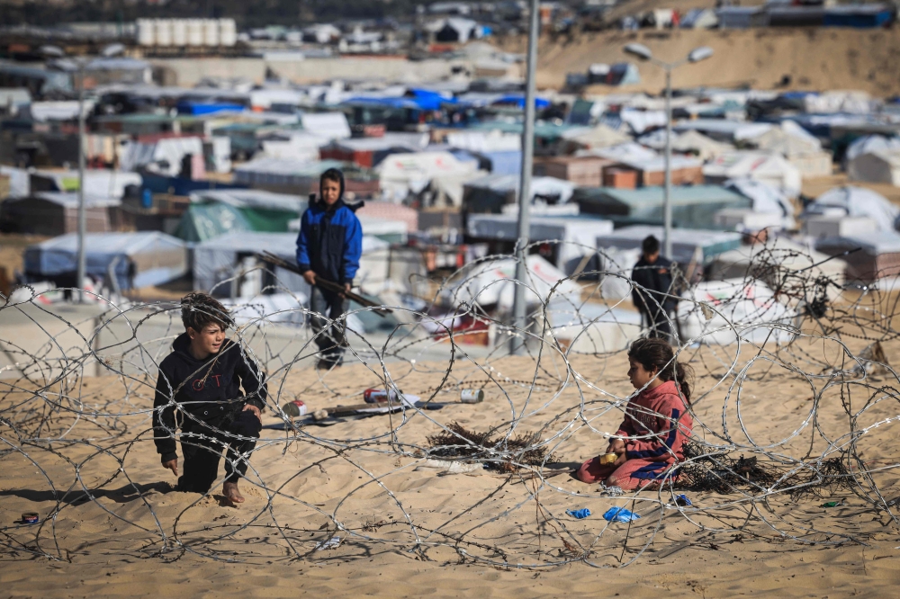 Displaced Palestinian kids play behind barbed wire on a sand dune overlooking a makeshift camp on the Egyptian border, west of Rafah in the southern Gaza Strip on January 14, 2024. (Photo by AFP)