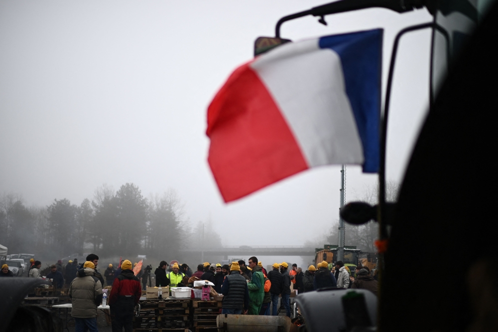 Farmers of the CR47 union (Coordination rurale 47), next to French flag on a tractor, attend a blocking of the A62 highway near Agen, southwestern France, on January 27, 2024.(Photo by Christophe ARCHAMBAULT / AFP)

