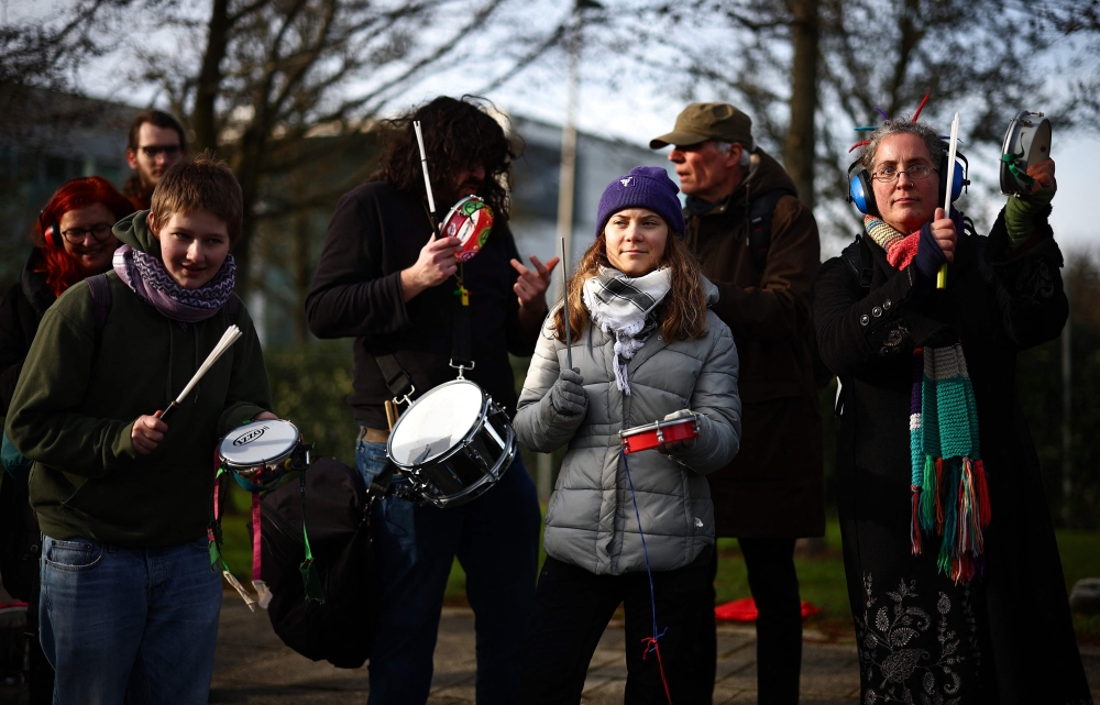 Swedish environmental activist Greta Thunberg (C) bangs a tambourine as she stands with members of the Extinction Rebellion (XR) climate change group, protesting against plans to increase private jet flights, at Farnborough Airport in Farnborough, west of London on January 27, 2024. (Photo by HENRY NICHOLLS / AFP)
