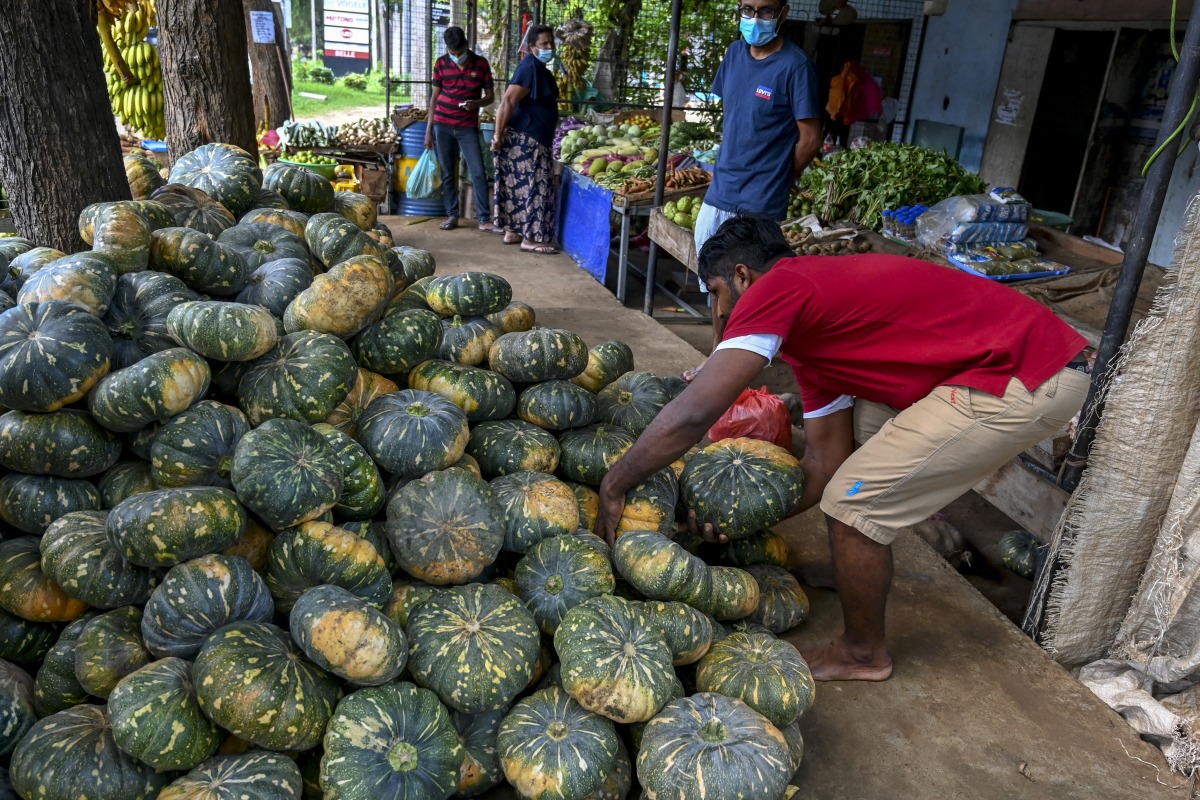 A vendor sorts pumpkins as customers buy vegetables in Hambantota on December 22, 2021. (Photo by ISHARA S. KODIKARA / AFP)
