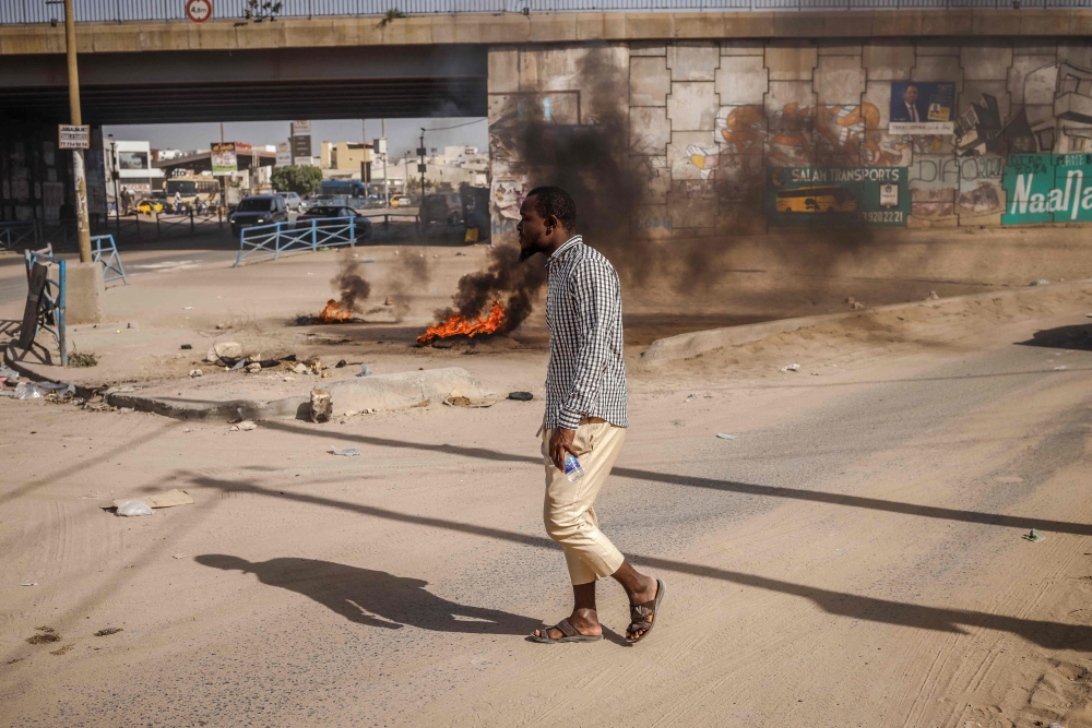 A man walks next to some burning tyres barricade following demonstrations called by the opposition parties in Dakar on February 4, 2024. (Photo by John Wessels / AFP)
