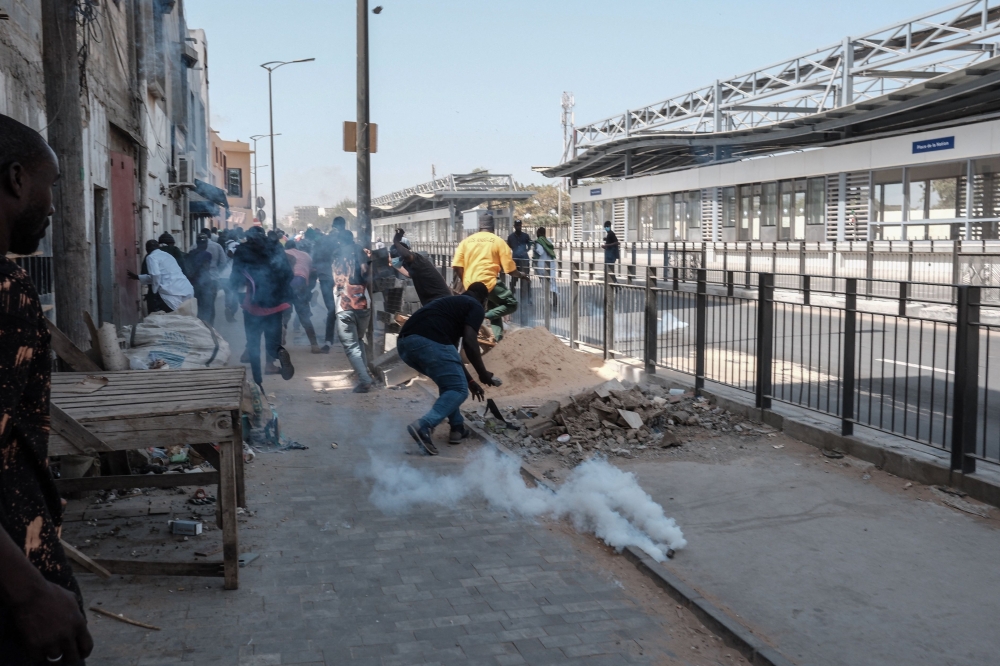 Protestors run away as a smoke grenade lands near them during clashes with police in Dakar on February 9, 2024. (Photo by GUY PETERSON / AFP)
