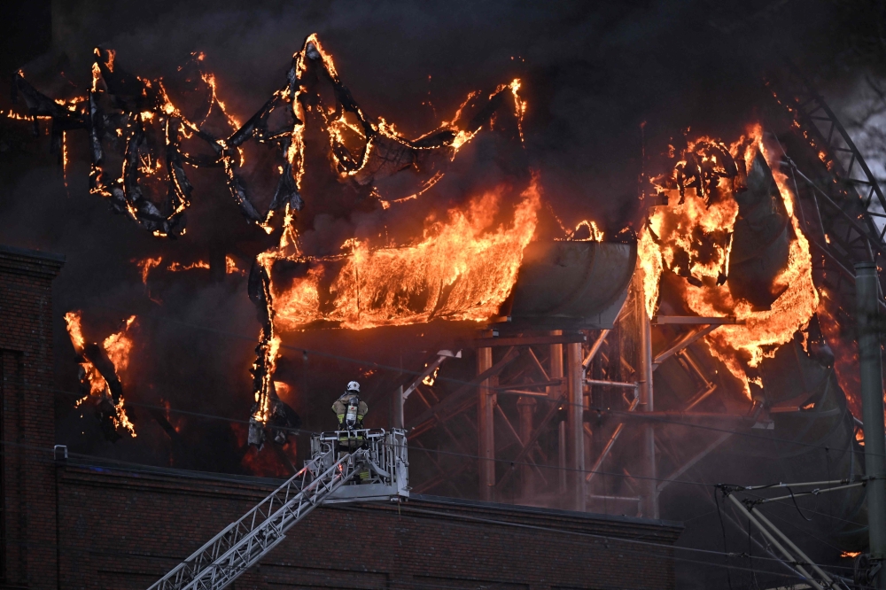 A firefighter is seen on an aerial ladder platform as a fire engulfs a structure of the Oceana Waterworld at the Liseberg Amusement Park in Gothenburg, Sweden on February 12, 2024. (Photo by Bjorn LARSSON ROSVALL / TT News Agency / AFP) 