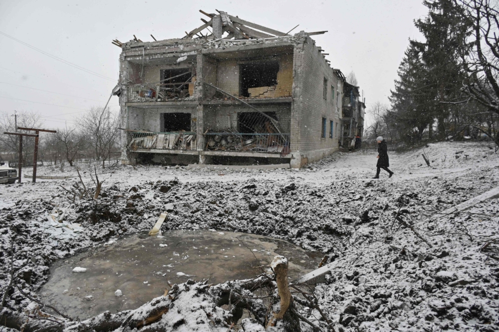 A local resident walks past a crater and a damaged residential building following a recent aerial bombardment in Kupiansk, Kharkiv region, on February 18, 2024, amid the Russian invasion of Ukraine. (Photo by SERGEY BOBOK / AFP)
