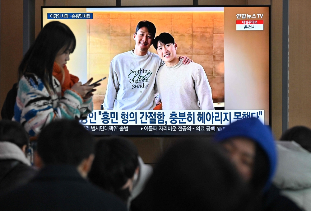 A woman walks past a television screen showing a news broadcast with a picture of Son Heung-min (L) and Lee Kang-in (R), at a railway station in Seoul on February 21, 2024. Photo by Jung Yeon-je / AFP