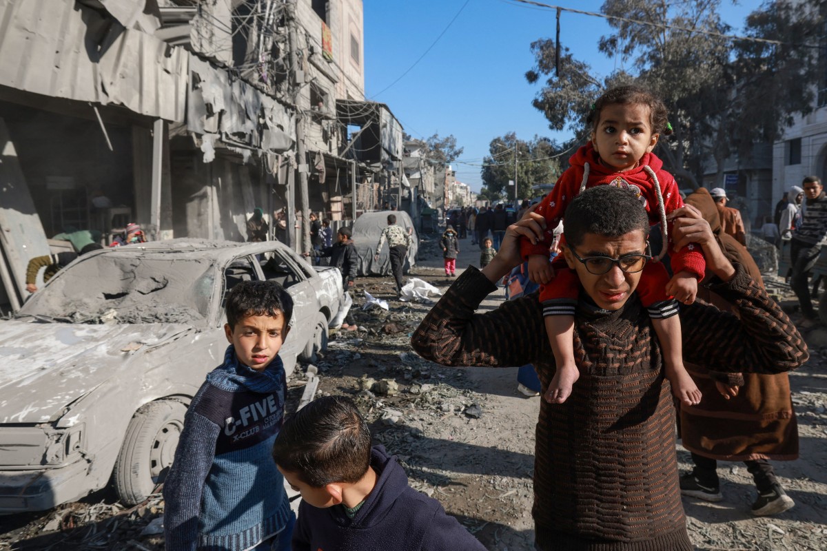 Palestinians walk past debris on February 22, 2024, following overnight Israeli air strikes in Rafah refugee camp in the southern Gaza Strip. (Photo by Mohammed Abed / AFP)