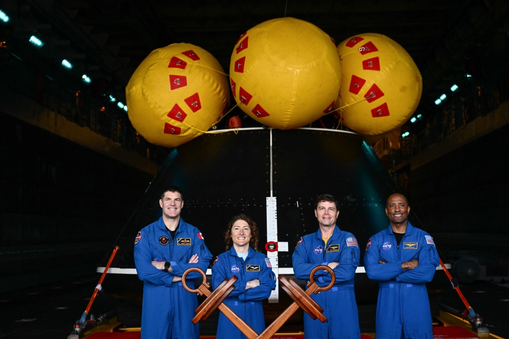(From left) Canadian Space Agency (CSA) astronaut Jeremy Hansen, NASA Astronaut Christina Koch, NASA Astronaut Reid Wiseman, and NASA Astronaut Victor J. Glover stand for a photograph in front of the Orion crew module test capsule in the well deck aboard the USS San Diego (LPD-22) at Naval Base San Diego following the Underway Recovery Test 11 in San Diego, California on February 28, 2024. (Photo by Patrick T. Fallon / AFP)