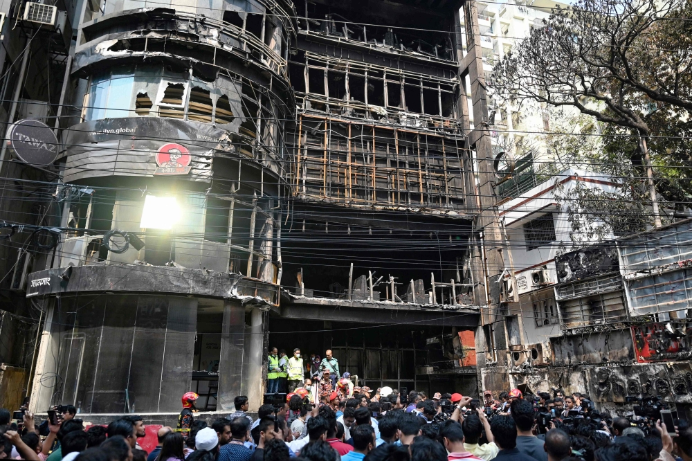 People gather near a commercial building a day after a fire accident, as firefighters and forensic expert inspect the site in Dhaka on March 1, 2024. Photo by Munir UZ ZAMAN / AFP