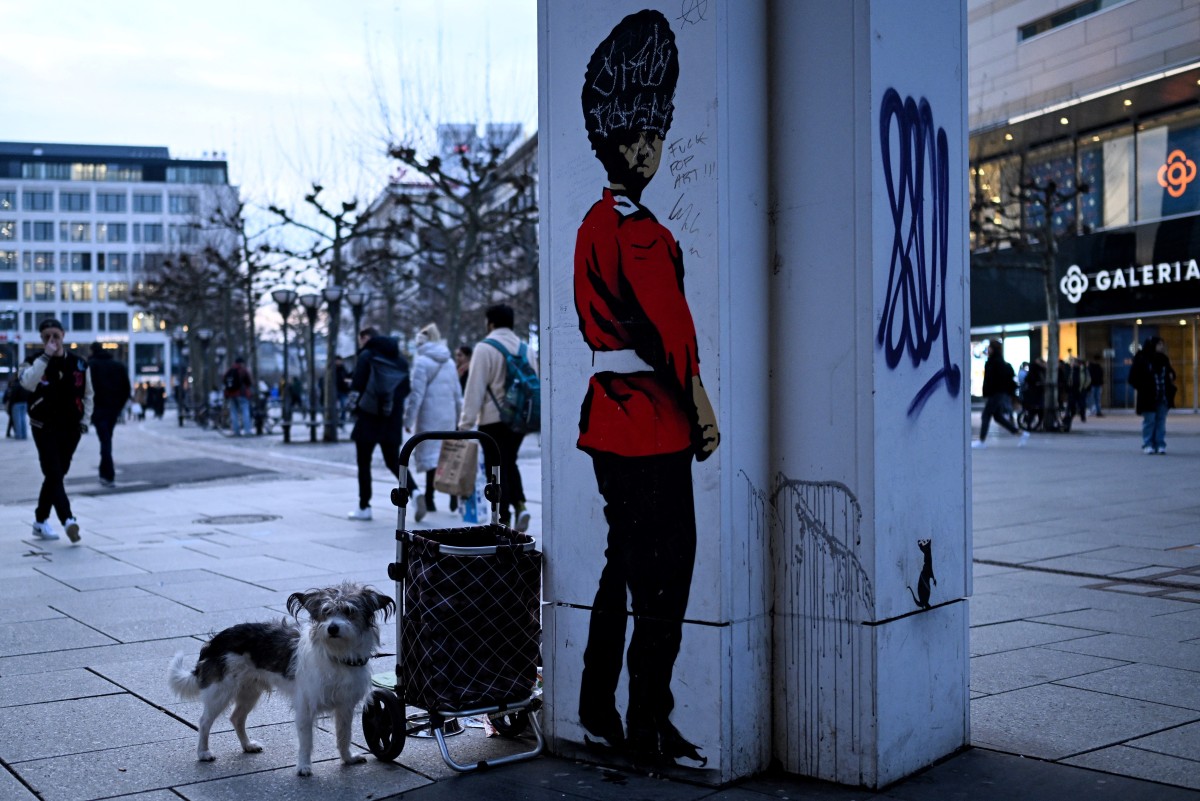 A dog stands next to a column with the mural of a London Guard on the main shopping street in Frankfurt am Main, western Germany, on February 28, 2024. (Photo by Kirill KUDRYAVTSEV / AFP)

