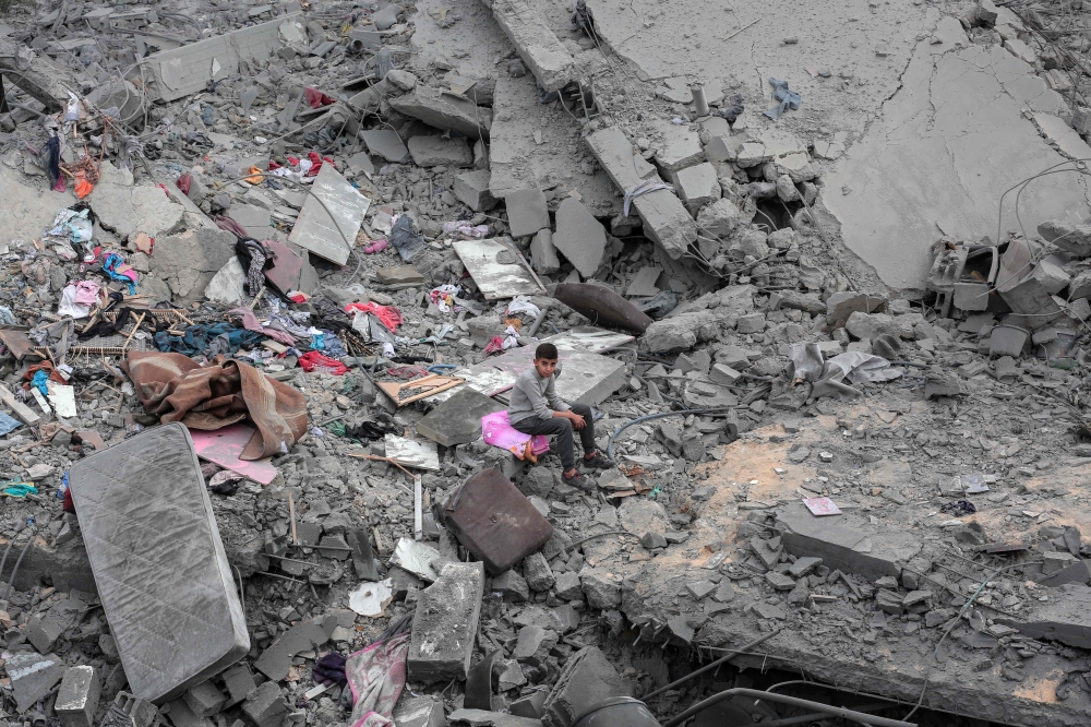 A boy sits among the rubble and scattered belongings of the Palestinian al-Atrash family, after their home was destroyed in an Israeli strike in Deir el-Balah in the central Gaza Strip on March 13, 2024, amid the ongoing conflict between Israel and the Palestinian Hamas group. (Photo by AFP)
