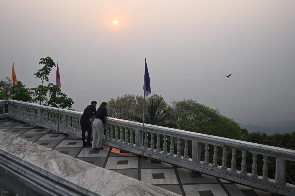 Tourists look out as high levels of air pollution obscure the view of Chiang Mai from atop Wat Phra That Doi Suthep temple on March 15, 2024. (Photo by Lillian SUWANRUMPHA / AFP)