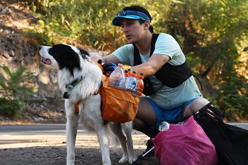Sportsman and lawyer Gonzalo Chiang accompanied by his pet Sam, pick up plastic bottles during a plog run at Cerro San Cristobal in Santiago, on March 12, 2024. Photo by RODRIGO ARANGUA / AFP