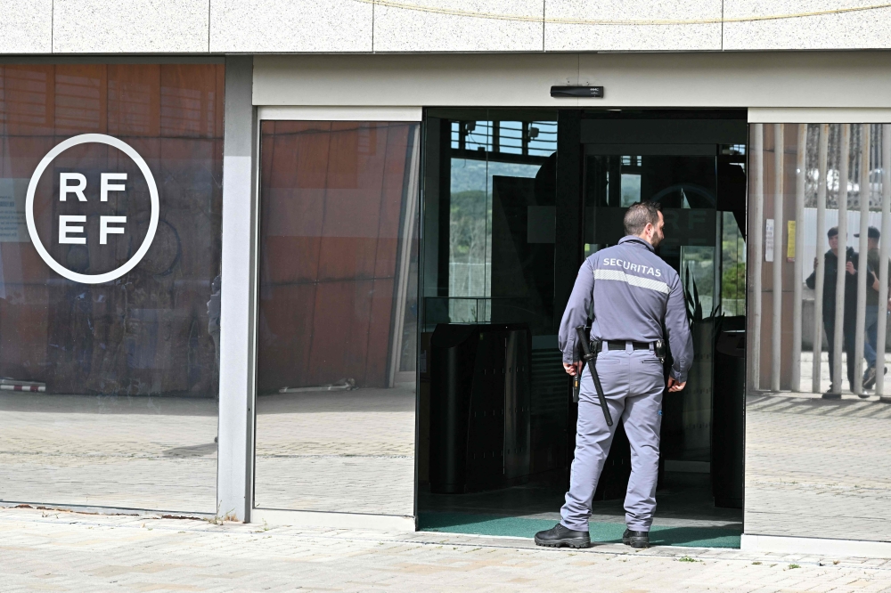 A security staff member stands as journalists wait outside the headquarters of the Spanish Royal Football Federation (RFEF) in Las Rozas de Madrid on March 20, 2024 during a police search. Photo Credit: JAVIER SORIANO / AFP.
