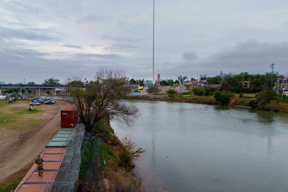In an aerial view, a National Guard soldier stands atop a barrier of shipping containers while patrolling at Shelby Park on March 20, 2024 in Eagle Pass, Texas. (Photo by Brandon Bell / GETTY IMAGES NORTH AMERICA / Getty Images via AFP)
