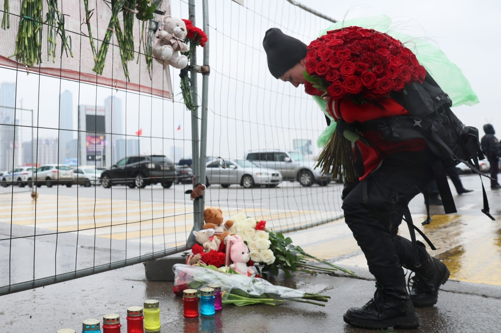 A woman lays flowers at a makeshift memorial in front of the Crocus City Hall, A day after a gun attack in Krasnogorsk, outside Moscow, on March 23, 2024. Photo Credit: STRINGER / AFP.