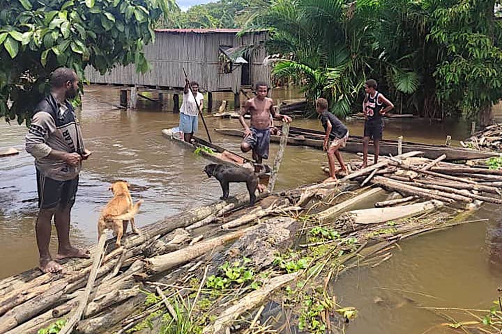 This photo released by the Papua New Guinea Police and received by AFP on March 25, 2024 shows locals on a makeshift bridge in the flooded Angriman Village in Angoram District, East Sepik, Papua New Guinea. (Photo by Handout / PNG Police / AFP) 