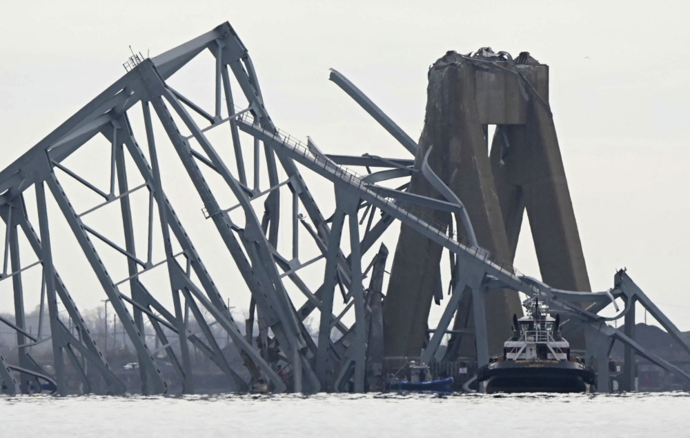 The steel frame of the Francis Scott Key Bridge lies in the water after it collapsed in Baltimore, Maryland, on March 26, 2024. Photo by Mandel NGAN / AFP.