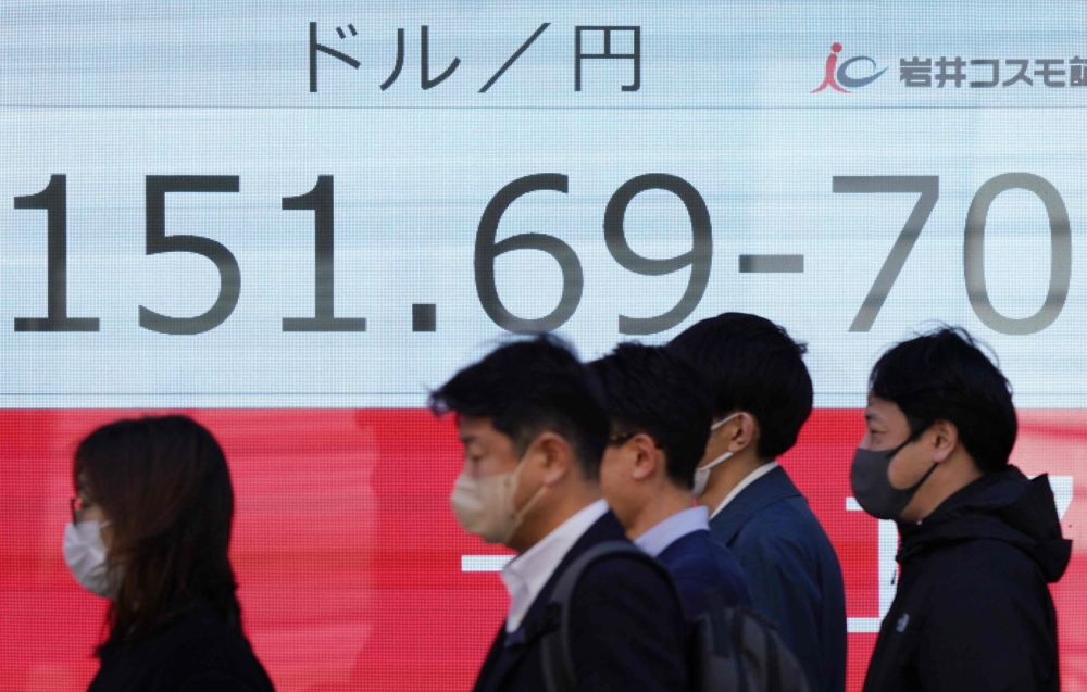 People walk past an electronic board showing the rate of the Japanese yen versus the US dollar along a street in Tokyo on March 27, 2024. Photo by Kazuhiro NOGI / AFP.