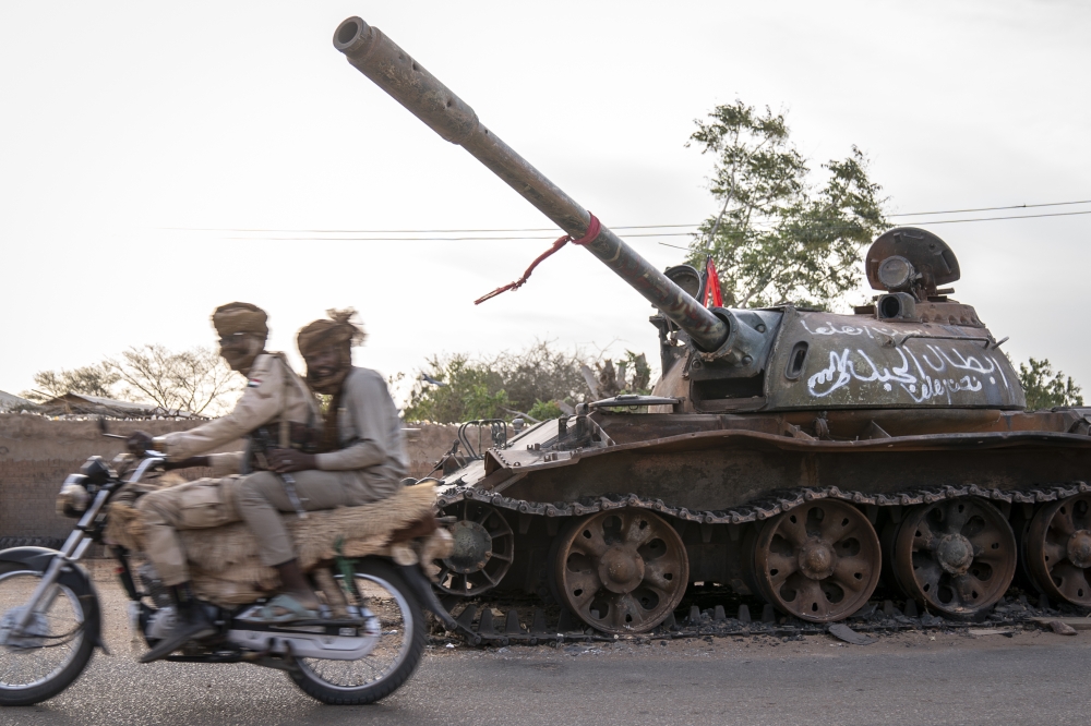 RSF soldiers ride a motorcycle on a main street in El Geneina past a destroyed tank that belonged to the Sudanese military. Photo by Diana Zeyneb Alhindawi