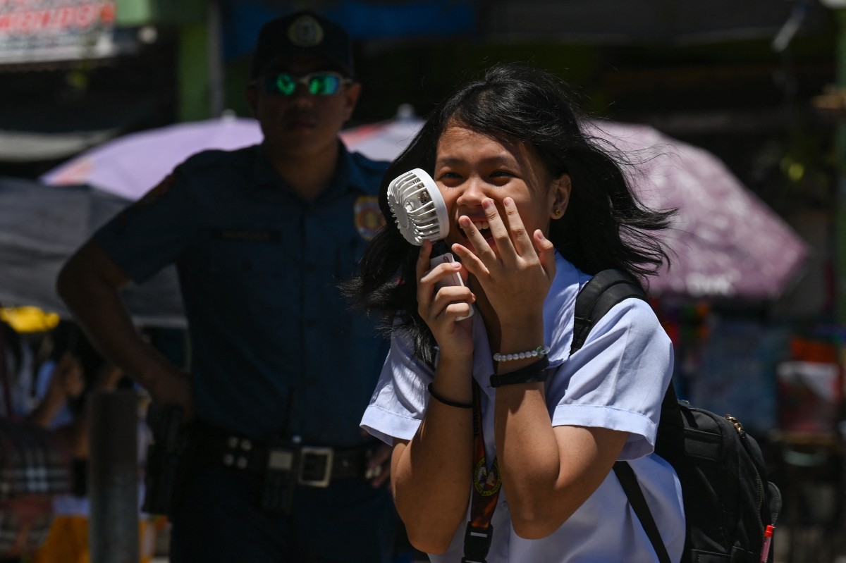 A student uses a portable fan outside a school in Manila on April 2, 2024. Photo by JAM STA ROSA / AFP