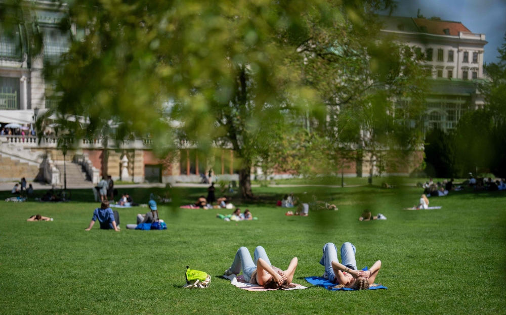 People enjoy the sunny and warm weather on a meadow at the public garden in Vienna on April 7, 2024. (Photo by GEORG HOCHMUTH / APA / AFP) / Austria OUT
