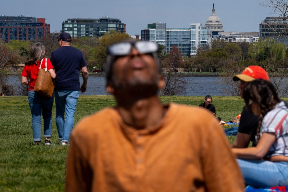 The Dome of the U.S. Capitol Building is visible as Johnny Marshall, of Brandywine, Maryland, (Foreground) views the partial solar eclipse at Gravelly Point Park on April 8, 2024 in Arlington, Virginia. (Photo by Andrew Harnik / GETTY IMAGES NORTH AMERICA / Getty Images via AFP)
