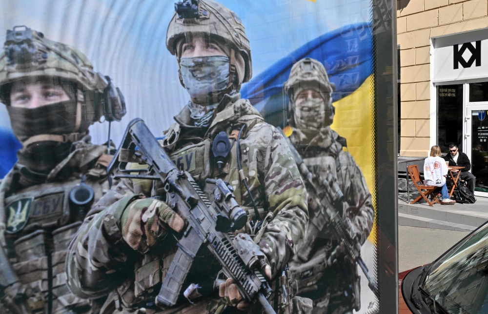 A couple sits outside a cafe next to a military recruiting poster in Kyiv, on April 9, 2024, amid Russia's invasion on Ukraine. (Photo by Sergei Supinsky / AFP)
