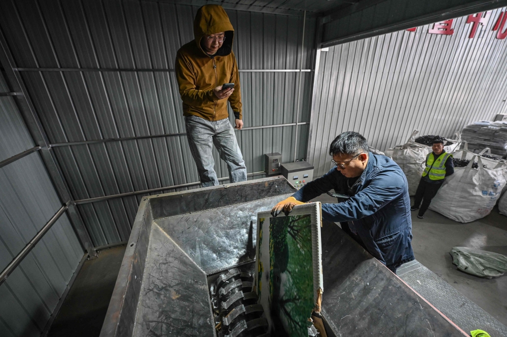 This photo taken on March 27, 2024 shows worker Yang Weiguang (R) placing a large wedding photo into a shredding machine as Liu Wei takes videos on the side at a warehouse in Langfang, in northern China's Hebei province. (Photo by Jade Gao / AFP) 