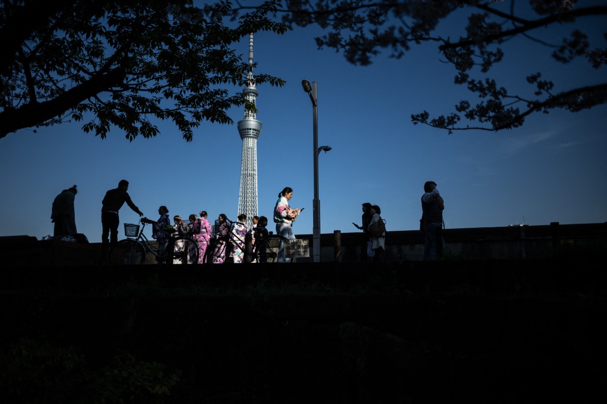 People gather under the blooming cherry blossoms with the background of the landmark Tokyo Skytree (C) at Sumida Park, near the famous tourism spot of Asakusa district in Tokyo on April 10, 2024. (Photo by Philip FONG / AFP)
