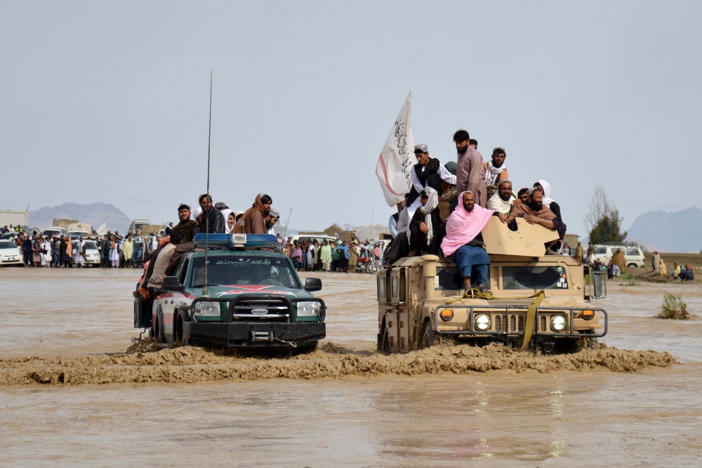 Afghan men sit atop of military vehicles as they cross through a flooded area in Spin Boldak district of Kandahar province on April 13, 2024, after a flash flood following a heavy rainfall. (Photo by Sanaullah SEIAM / AFP)
