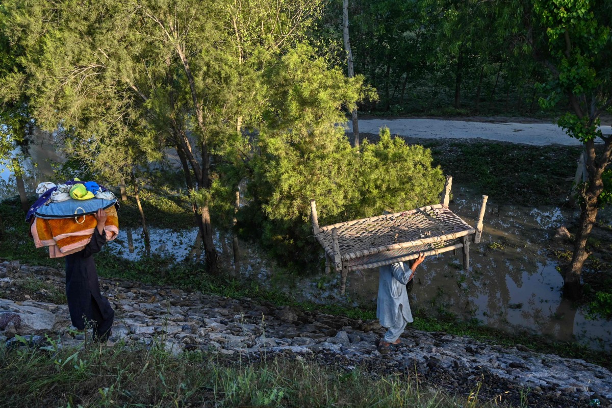 A displaced family carry their belongings to tents at a makeshift camp after fleeing from their flood hit homes following heavy rains in Charsadda district of Khyber Pakhtunkhwa province on April 17, 2024. (Photo by Abdul MAJEED / AFP)