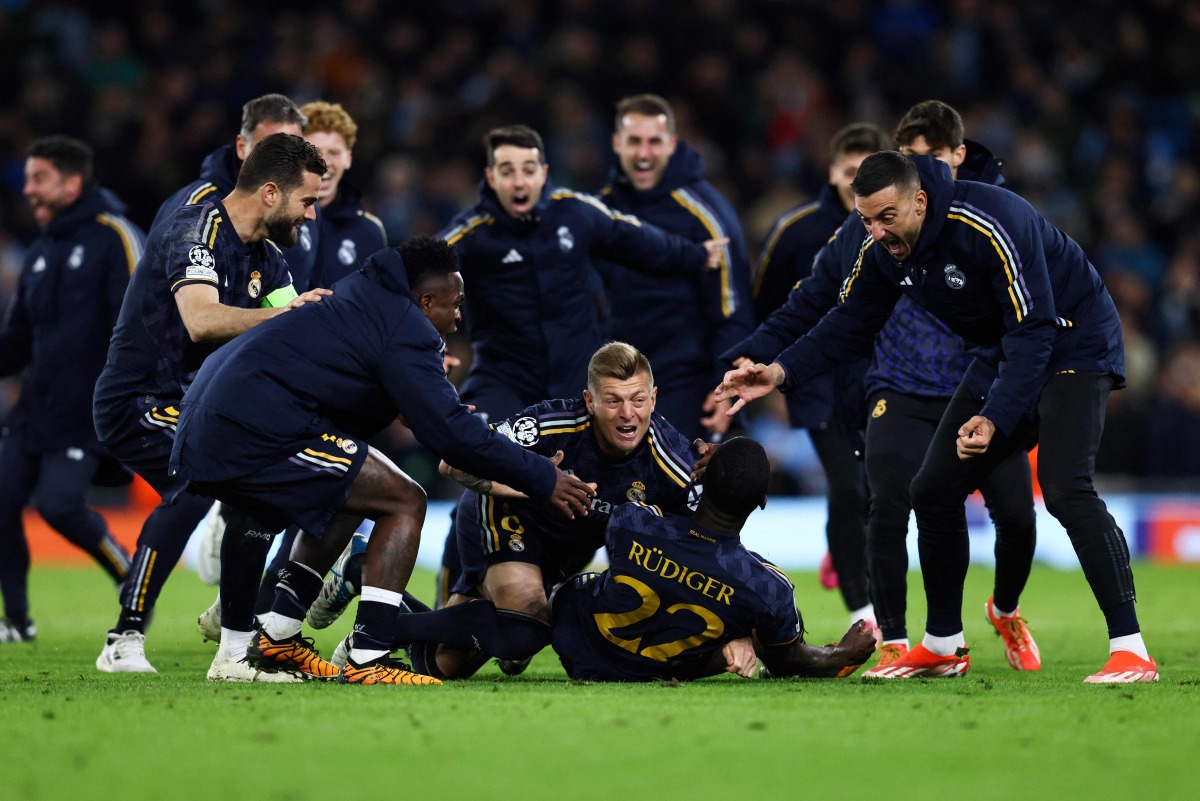 Real Madrid's German defender #22 Antonio Rudiger celebrates with teammates after scoring the winning penalty during the penalty shootout during the UEFA Champions League quarter-final second-leg football match between Manchester City and Real Madrid, at the Etihad Stadium, in Manchester, north-west England, on April 17, 2024. (Photo by Darren Staples / AFP)