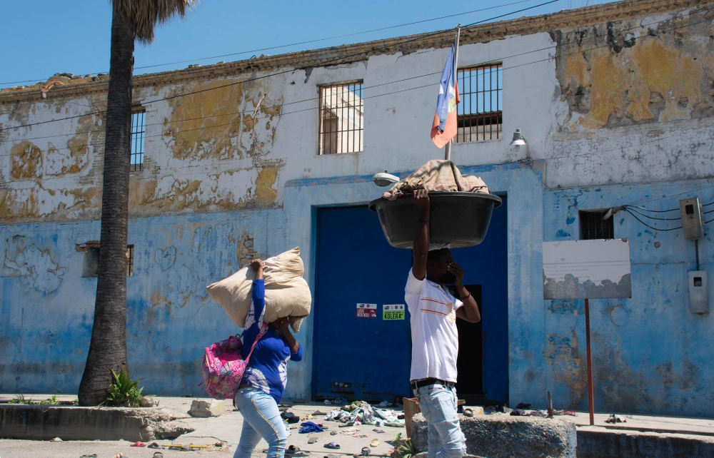 People walk with their hands over their faces to protect themselves from the stench of decomposing bodies as they pass the National Penitentiary in Port-au-Prince, Haiti, March 4, 2024. (Photo by Clarens Siffroy / AFP)