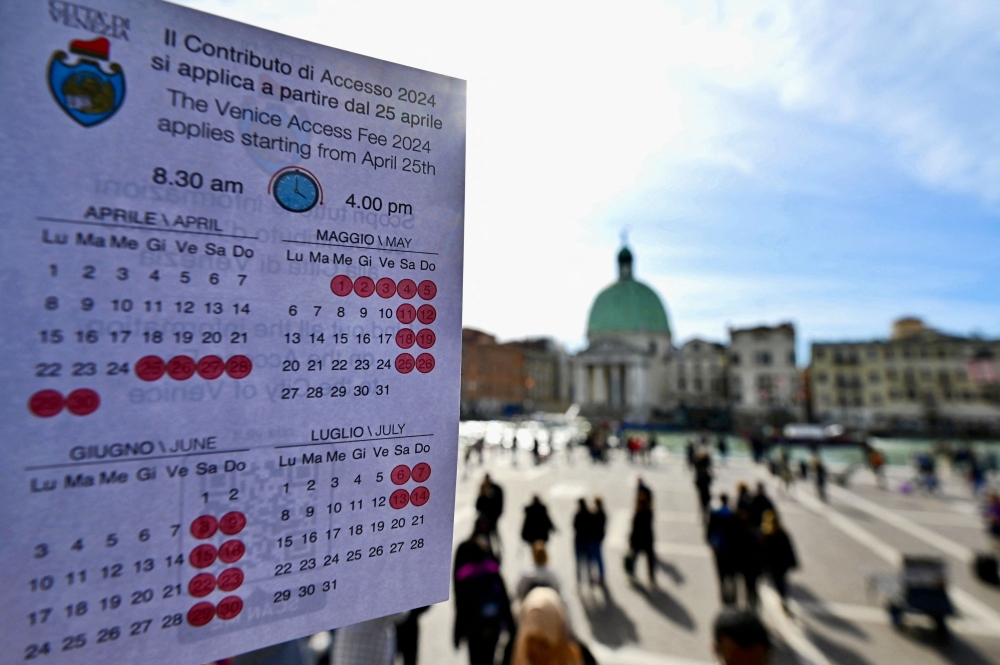 A person shows a calendar of the paying days to visit Venice, on April 19, 2024 in front of Santa Lucia train station in Venice. (Photo by Gabriel Bouys / AFP)