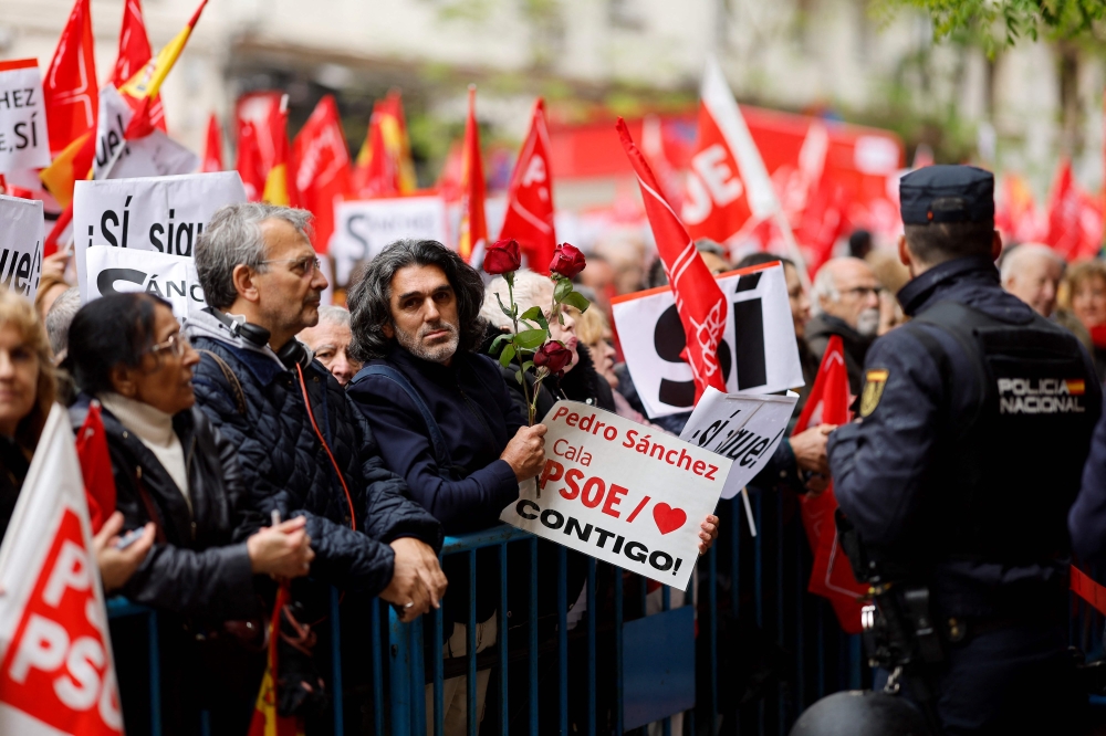 A protestor holds a sign and roses during a demonstration called in support of the Spanish Prime Minister, in front of the PSOE party headquarters in Madrid, on April 27, 2024. (Photo by OSCAR DEL POZO / AFP)
