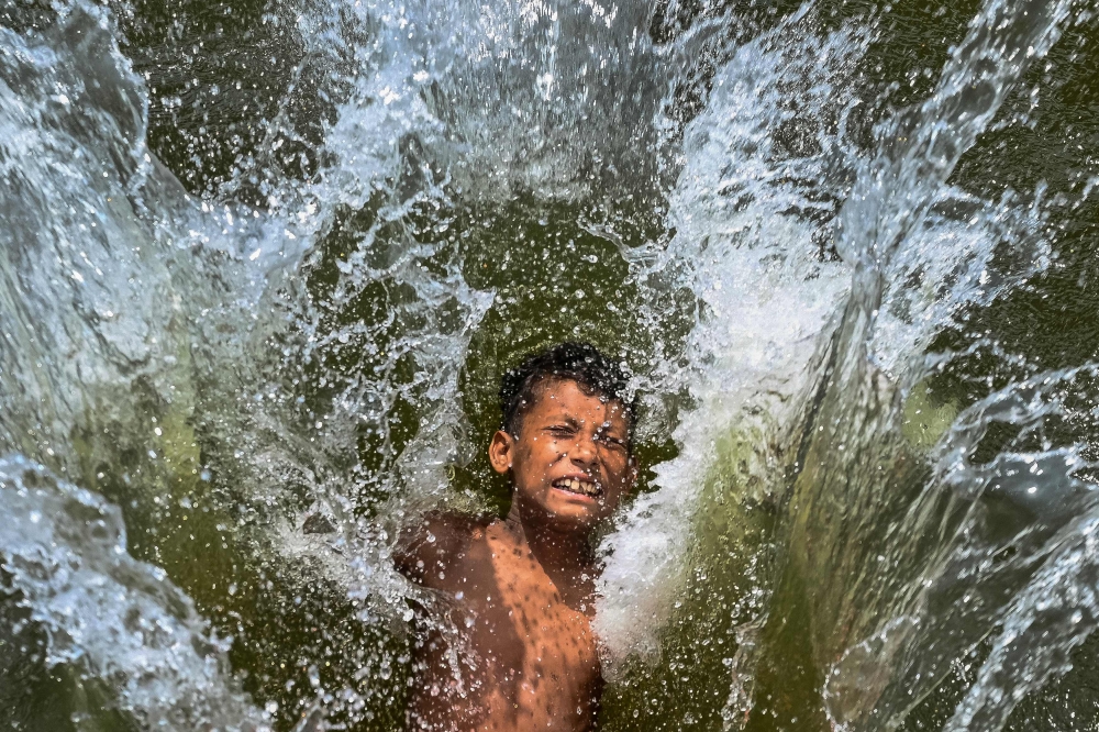 A child playfully takes a dip in a lake to get respite from the heat on a summer afternoon in Dhaka on April 29, 2024. (Photo by Munir Uz Zaman / AFP)
