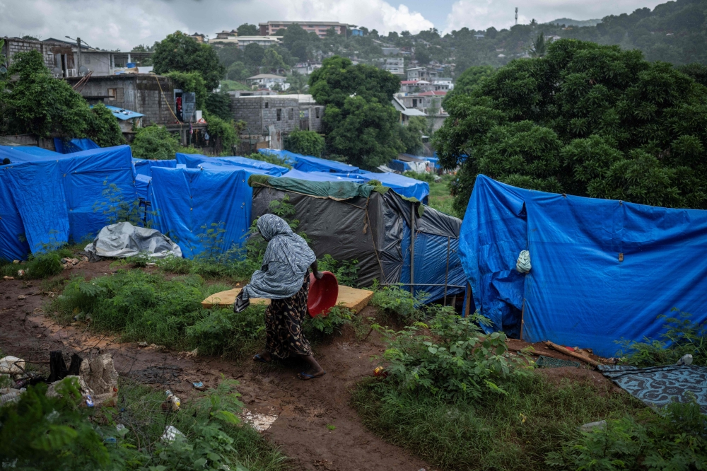 (FILES) A woman walks on a muddy pathway along shelter tents in a makeshift camp where migrants live at the Cavani stadium in Mamoudzou on the French island of Mayotte, on February 15, 2024. (Photo by JULIEN DE ROSA / AFP)
