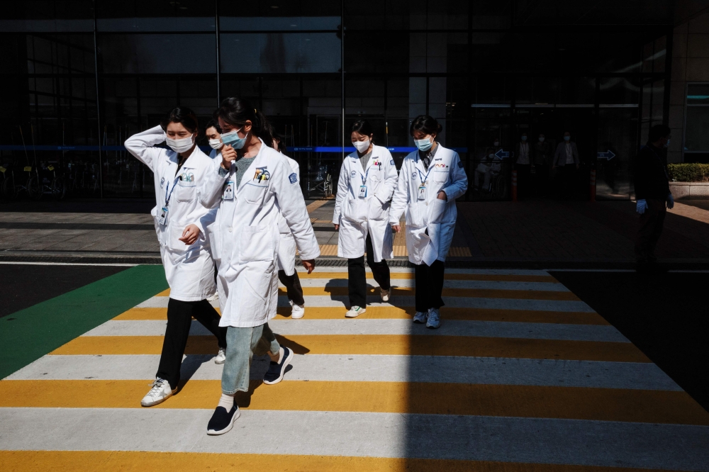 Medical workers walk across a pedestrian crossing outside a hospital in Seoul on March 11, 2024. Photo by Anthony WALLACE / AFP