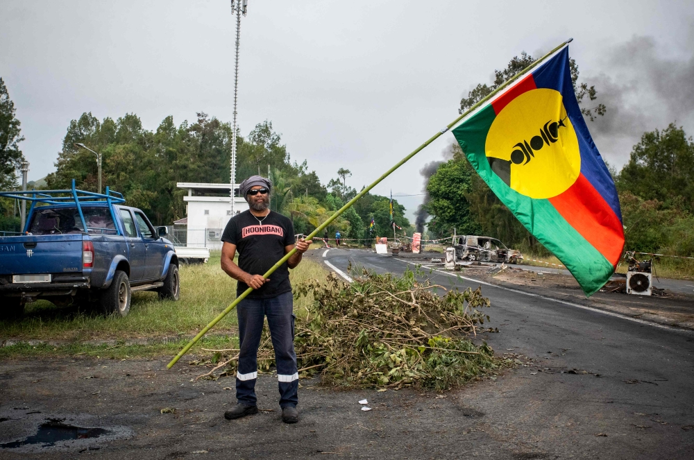 The resident in charge of the independantist roadblock at La Tamoa, holds a Kanak flag in the commune of Paita, France's Pacific territory of New Caledonia on May 19, 2024. Photo by Delphine Mayeur / AFP.