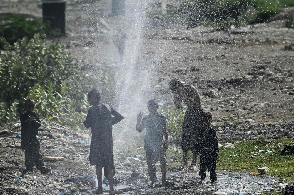 Youths cool off as water bursts out from a damaged water pipe line amidst a heatwave in Karachi on May 21, 2024. (Photo by Asif HASSAN / AFP)