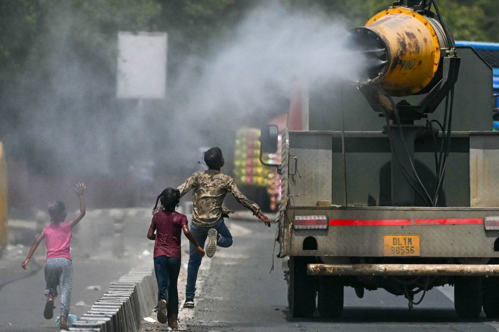 Children run behind a truck spraying water along a street on a hot summer day in New Delhi on May 28, 2024. (Photo by Arun Sankar / AFP)
 