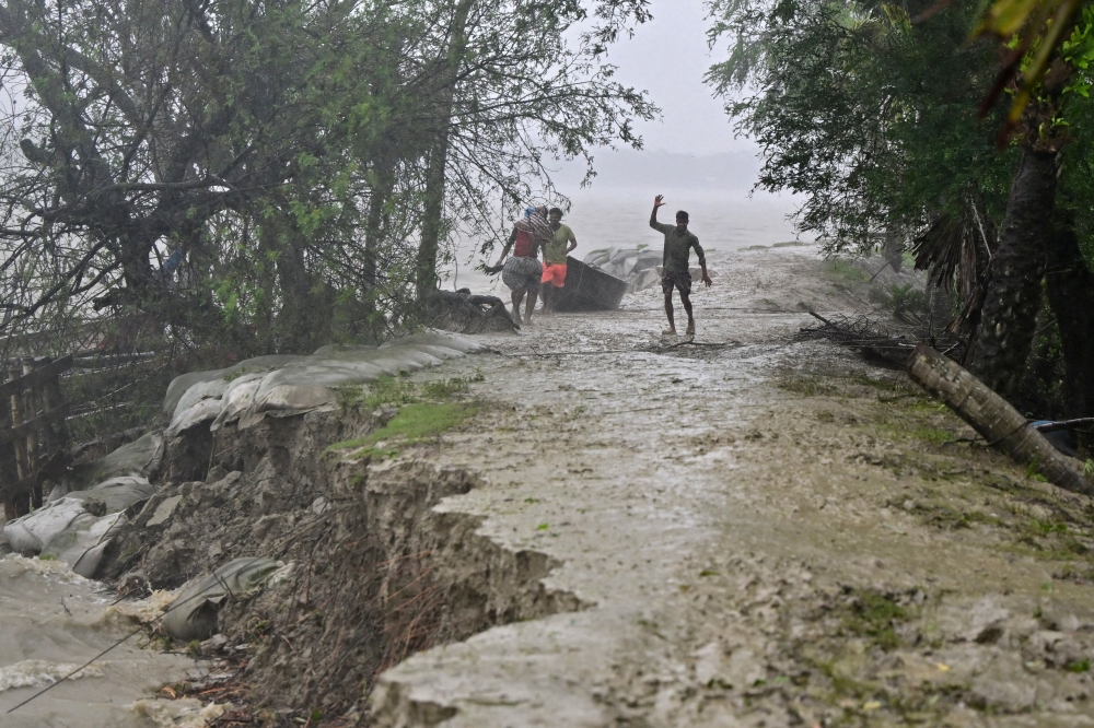 People walk on a damaged embankment along the Sonatola river during heavy rainfall in Patuakhali on May 27, 2024, following the landfall of Cyclone Remal in Bangladesh. Photo by Munir Uz Zaman / AFP