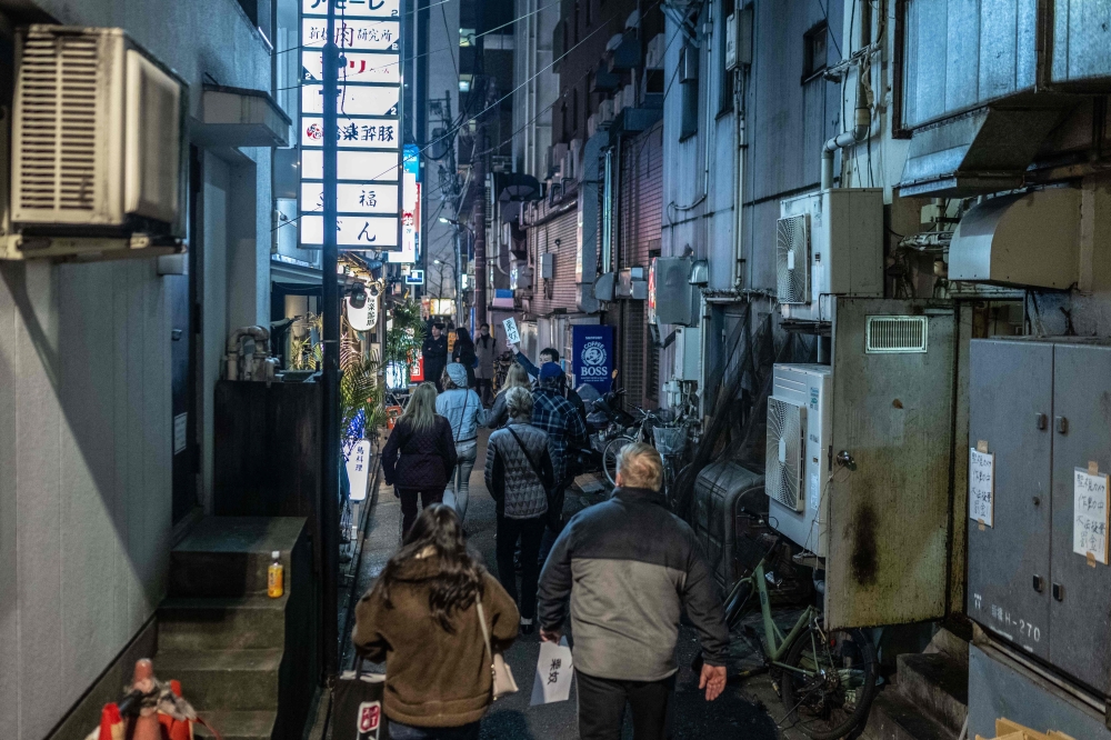This picture taken on March 22, 2024 shows tourists from the US walking down a small alleyway as they take part in a snack bar tour in Tokyo. Photo by Yuichi YAMAZAKI / AFP