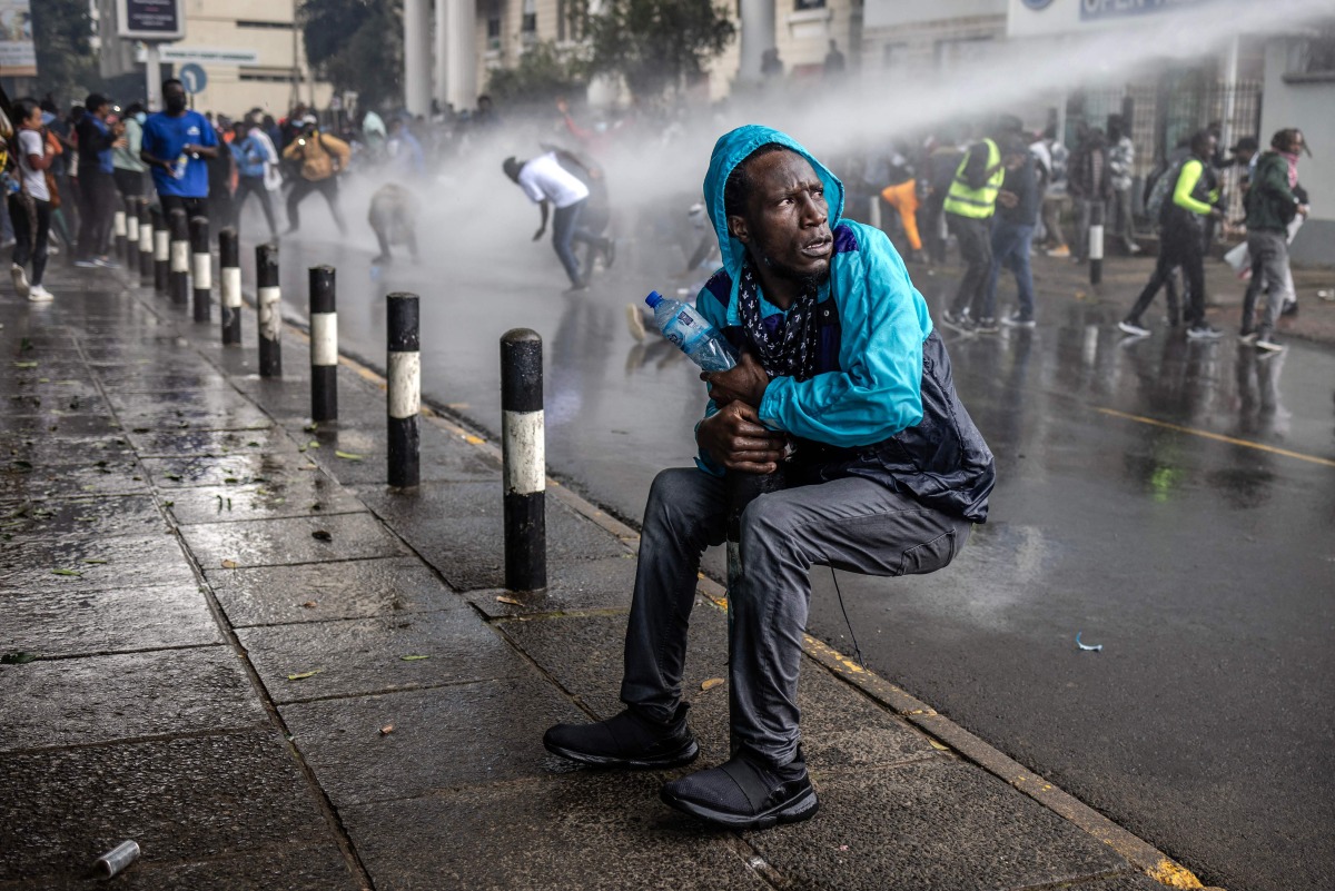 A protester reacts as a Kenyan police water canon sprays water at them during a demonstration against tax hikes in downtown Nairoibi, on June 20, 2024. (Photo by Luis Tato / AFP)