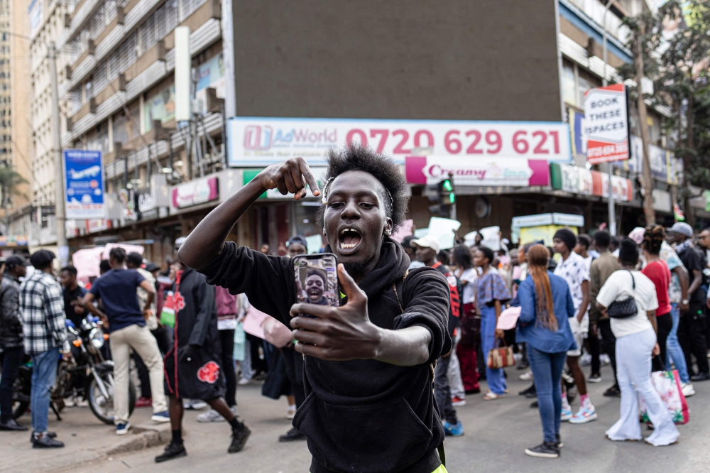 A man uses his phone to record a live video on social media while marching against the Finance Bill 2024 in downtown Nairobi on June 23, 2024. (Photo by Patrick Meinhardt / AFP)