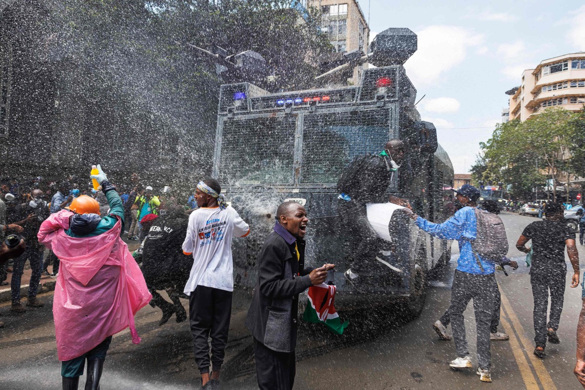 Protesters are perched on a police water cannon as it attempts to repel them with chemically treated water jets during a nationwide strike to protest against tax hikes and the Finance Bill 2024 in downtown Nairobi, on June 25, 2024. (Photo by Tony KARUMBA / AFP)
