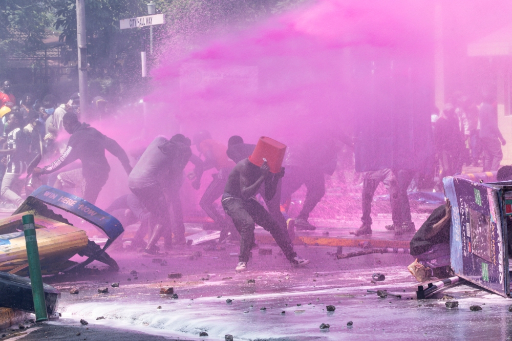 A protester tries to protect himself from the water thrown up by police cannons during a demonstration in Nairobi, on June 25, 2024. (Photo by Simon Maina / AFP)
