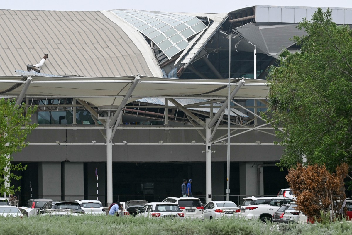 People walk past the collapsed terminal roof of New Delhi's Indira Gandhi International Airport after heavy rains in New Delhi on June 28, 2024. Photo by Arun SANKAR / AFP.
